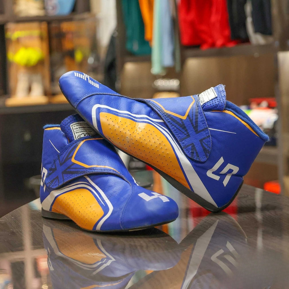 Blue and orange Lando Norris 2021 F1 Racing boots with 'LR' branding on a reflective surface.