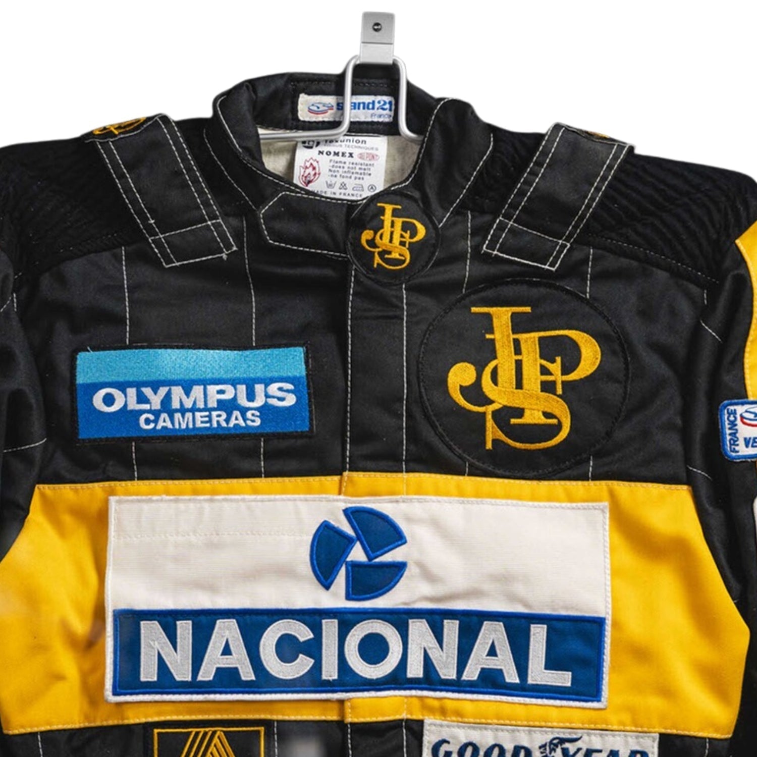 Close-up detail of the Ayrton Senna 1985 F1 racing suit fabric and stitching, showcasing vintage craftsmanship and sponsor detailing.