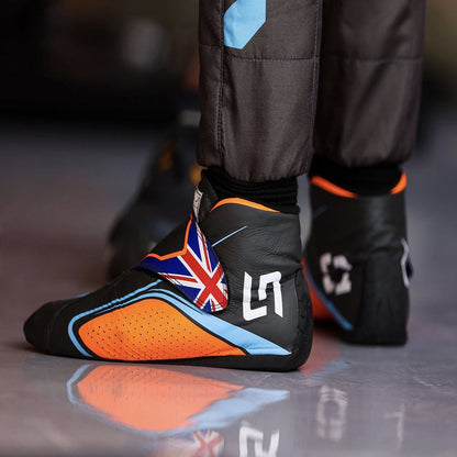 Black and orange Lando Norris 2022 F1 racing shoes with British flag design on a reflective surface.