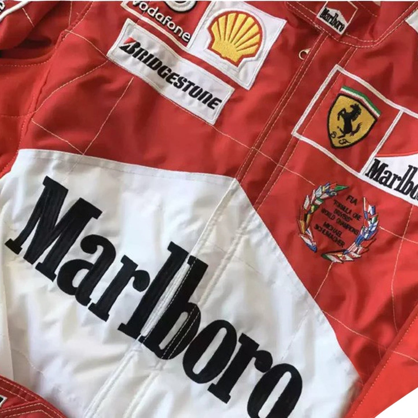 Close-up of the 2005 Schumacher suit highlighting fine embroidery, Ferrari red color tone, and precise stitching on race-worn sponsor badges.