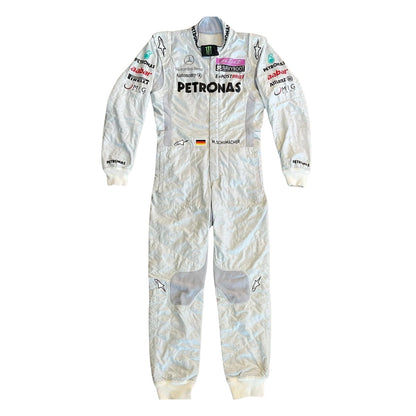 Front view of Michael Schumacher’s 2011 F1 racing suit in silver with green highlights, showcasing sponsor patches, front zip, and signature detailing.