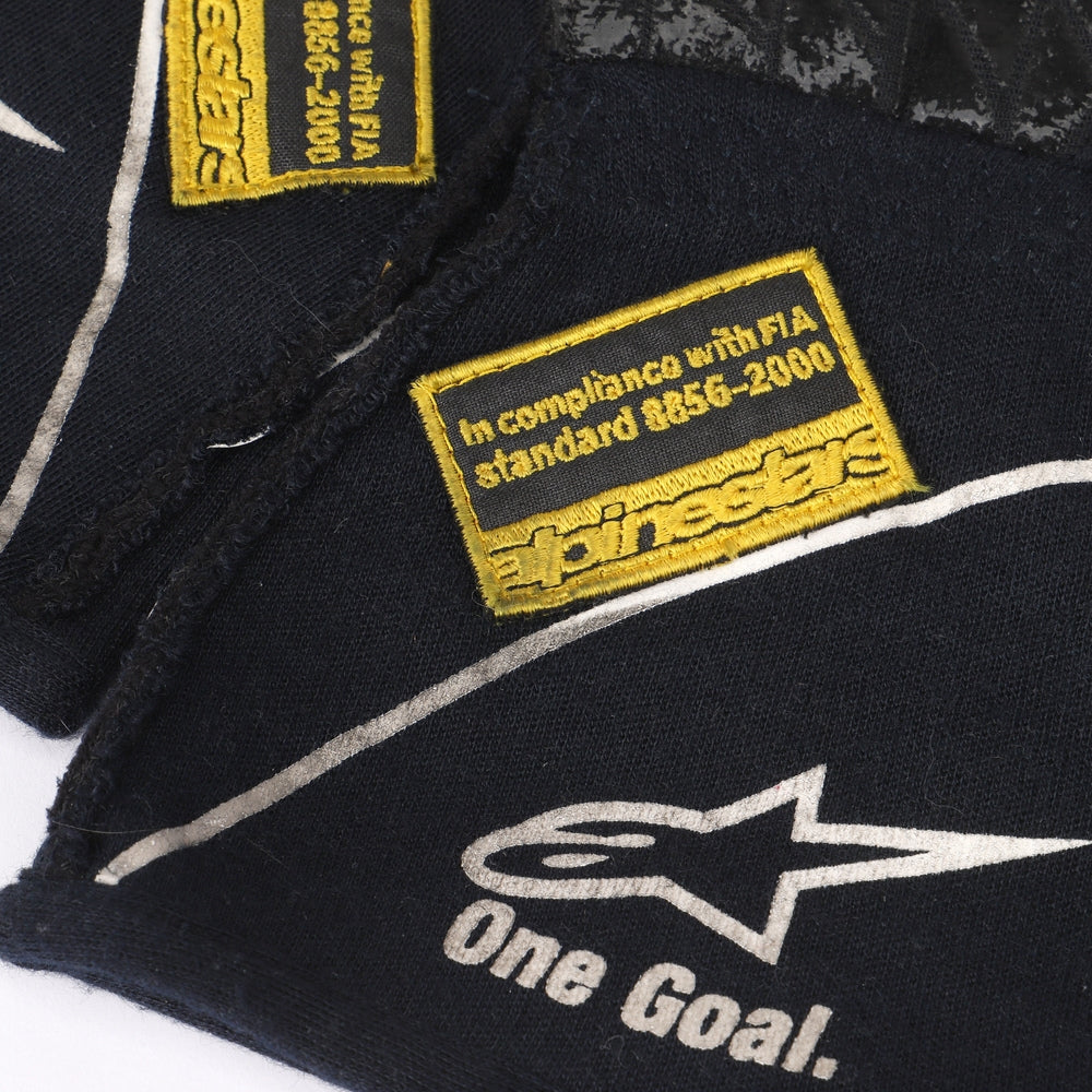 Close-up of a Valtteri Bottas 2015 black glove with yellow and white text and logos, including 'Alpinestars' and 'One Goal.'